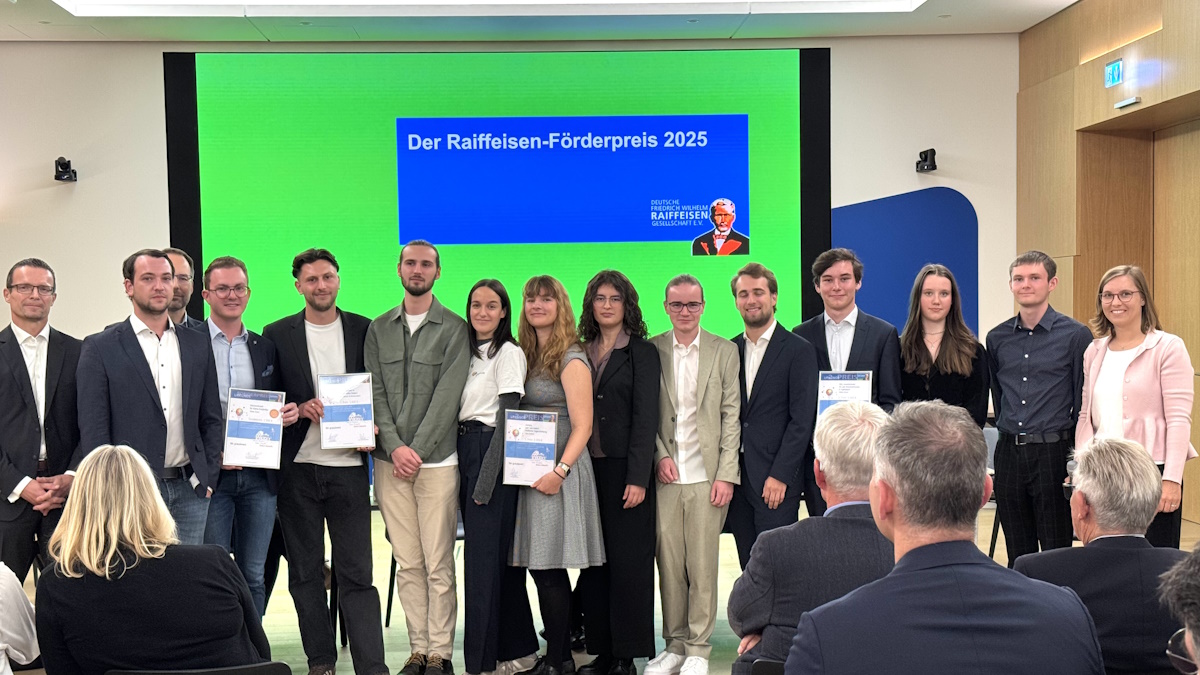 Menschen, die zusammenstehen, einige von ihnen halten Auszeichnungen oder Urkunden in den Händen. Im Hintergrund ist eine grüne Wand mit einem hellblauen Banner, worauf "Der Raiffeisen-Förderpreis 2023" steht. 